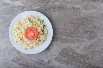 Slice tomatoes with farfalle pasta on the plate , on the marble background