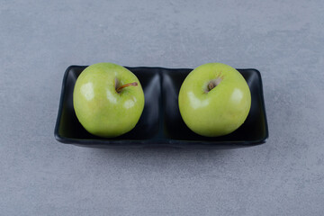 Two fresh green apple on black plate over grey background