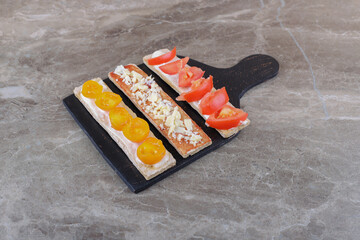 Sliced ripe and unripe tomatoes on crispy breads on the cutting board, on the marble background