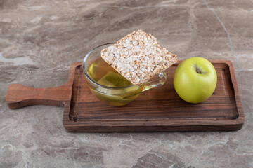 A piece of puffed rice cake, tea and apple , on the wooden tray, on the marble background
