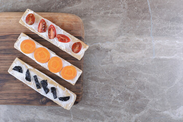 Sliced carrots, prunes and tomatoes on crispy breads, on the marble background