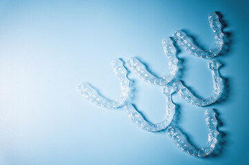 invisible plastic braces lie in reverse inverted pyramid shape in a row on a blue background, studio shot, nobody