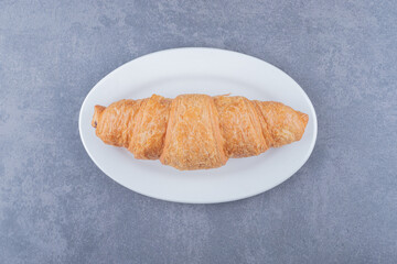 Freshly baked French croissant on white plate over grey background