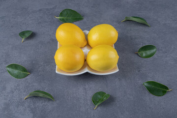 Close up photo of fresh lemons and leaves on grey background