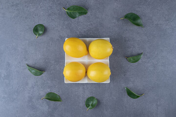 Four fresh organic lemons on white plate with leaves