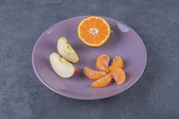 Season fruits. Apple, orange and tangerine slices on purple plate