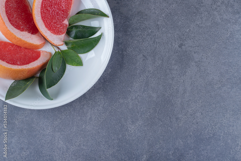 Wall mural Fresh Grapefruit slices and leaves on white plate