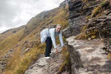 Naklejka na ściany i meble Adult woman walks on slippery stones in the mountains, austrian alps