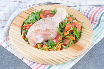 Raw chicken drumstick and sliced vegetables on wooden plate