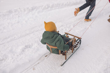 Father ridding his little son on a sled in a snowy forest. Holiday atmosphere. Winter family activities.