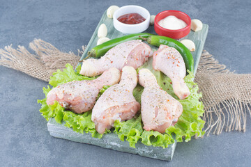 Uncooked chicken legs and chili peppers on wooden board