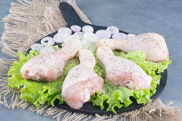 Uncooked chicken legs and sliced onion on black board
