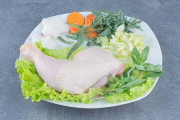 Raw chicken legs with vegetables on white plate