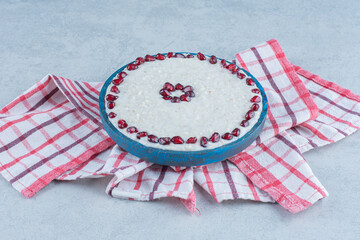 Obraz premium Pomegranate arils on porridge in the wooden plate, on towel, on the marble background