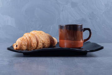 Cup of black coffee and croissant for breakfast on grey background