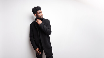 Serious young bearded guy in black clothes looking away while standing against white background