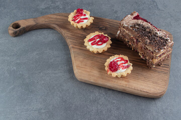 A piece of tasty cake and mini cupcakes on a wooden board