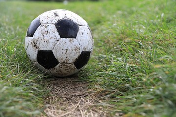 Dirty soccer ball on green grass outdoors, space for text