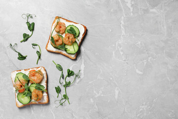 Tasty toasts with cream cheese, shrimps, cucumbers and microgreens on grey marble table, flat lay. Space for text
