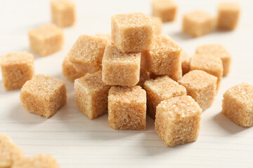 Heap of brown sugar cubes on white wooden table, closeup