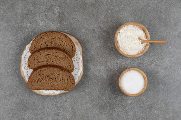 Black bread slices on wood piece with salt and flour