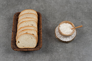 White bread slices in wooden basket with bowl of flour