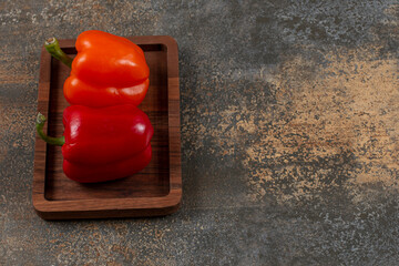 Orange and red sweet peppers in the board, on the marble background