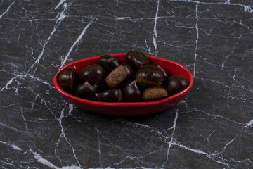 Toothsome chestnut in the red bowl, on the marble background