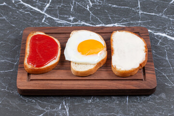 Fried eggs, jam and cheese on individually sliced bread on the board , on the marble background