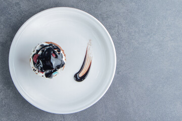 A white plate with delicious creamy cupcake on a gray background