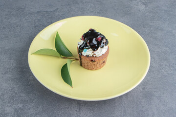 An yellow plate with delicious creamy cupcake on a gray background