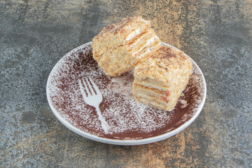 A white plate with two pieces of Napoleon cake and cocoa powder