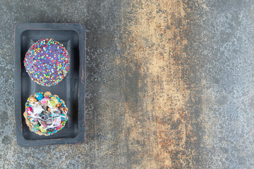 A dark wooden board of two cakes with colorful sprinkles