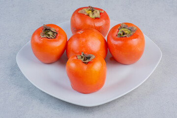 Ripe orange persimmon fruit on white plate