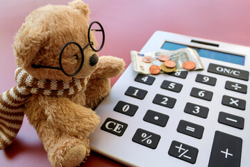 Small teddy bear in eyeglasses using calculator for calculating money 