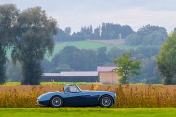 Oldtimer vintage luxury roadster sports car in a picturesque landscape. Vintage cabrio on a country road on a sunny summer day. Retro travel, traffic concept.