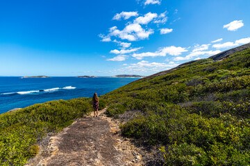 a long-haired girl in a dress stands at the top of a mountain admiring the view of a vast bay of white sand and turquoise water in cape le grand national park