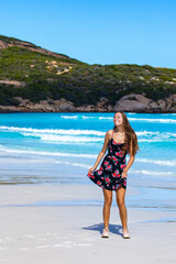 a long-haired girl in a black dress with roses dances on a paradise beach with white sand and turquoise water and orange rocks, cape le grand national park near esperance, western australia