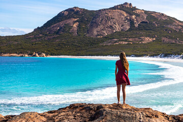 a long-haired girl in a dress walks along a paradise beach with white sand and turquoise water and orange rocks, cape le grand national park near esperance, western australia