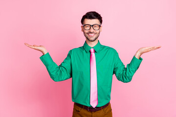 Portrait of young smiling guy wear green shirt hold hand comparsion prices shop isolated on pink color background
