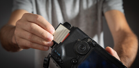 Photographer holding memory card insert DSLR camera.