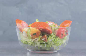 A bowl of salad with sausage, on the marble background