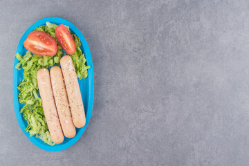 Tomato, sausage in lettuce leaves on the board , on the marble background