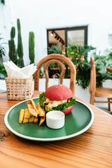 Vegan burger, in a red bun, dish with chips, on a green plate, on a wooden table, healthy vegetarian food.