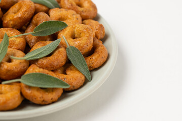 Traditional italian snacks taralli or tarallini with sage leaves in plate isolated on white background, close-up