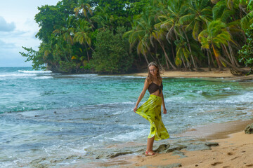 beautiful girl in yellow skirt walks on the caribbean beach in costa rica; wet season in costa rica, palms on the beach; paradise tropical beach