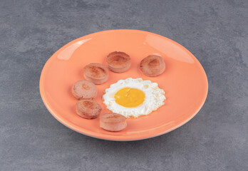 Fried egg and sliced sausage on the plate, on the marble background