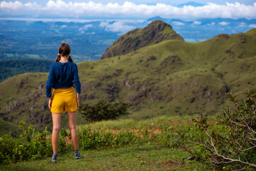 Fototapeta premium woman in hiking boots watching the view from the top of the mountain in costa rica, cerro pelado; brave hiker girl enjoying the view from the top after a hard hike