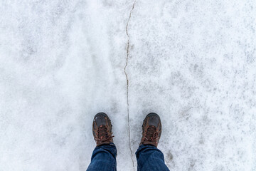 Male feet stand on a snowy ice with crack