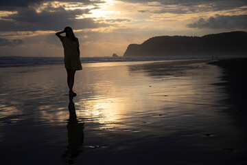 silhouette of a beautiful woman in a long dress with a colourful sunset on a tropical beach in the...